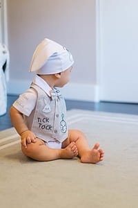 baby sitting on gray textile near white wall thumbnail