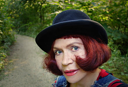 woman walking on pathway surrounded by green leafed plants while taking a selfie thumbnail