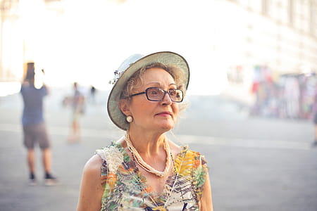 Close-up Of Old Aged Woman In Pastel Color Top, Sunhat And Spectacles Walking on the street thumbnail