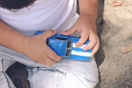 boy holding white and teal car die-cast model while sitting on gray concrete pavement thumbnail