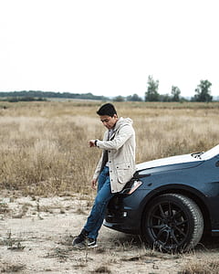man leaning on car while looking at his watch thumbnail
