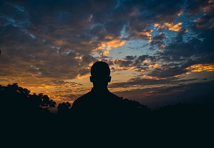 silhouette of man standing under white clouds at golden hour thumbnail