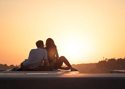 photo of man and woman sitting on sea shore during sunset thumbnail