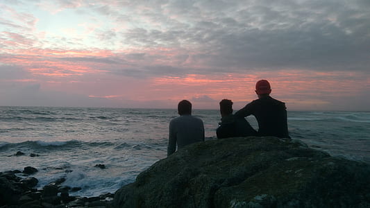 silhouette of people sitting on rock near shore thumbnail
