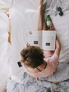 Woman in Pink Dress Sitting on Bed While Reading thumbnail