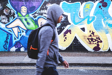 A man with a hooded-top and rucksack walks past the graffiti-covered streets of Shoreditch in East London thumbnail