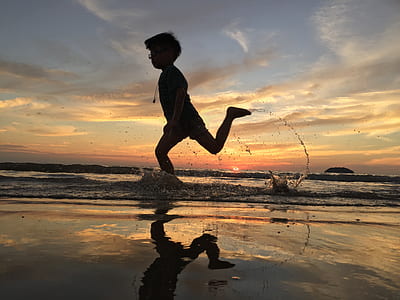 silhouette of boy running on body of water during sunset thumbnail