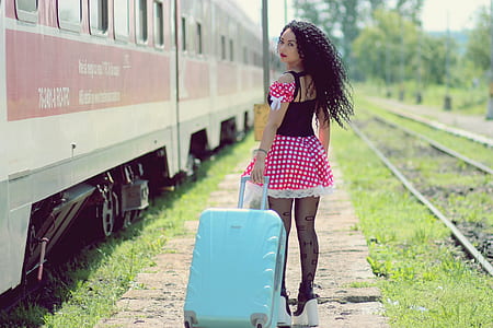 woman wearing red, white, and black polka-dot dress pulling teal luggage thumbnail