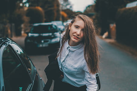 woman in gray dress shirt standing near black car thumbnail
