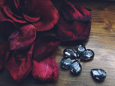 onyx gemstones near red Rose petals place on beige wooden surface in closeup photography thumbnail
