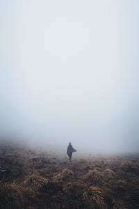 person wearing cape standing on brown ground soil under fog thumbnail