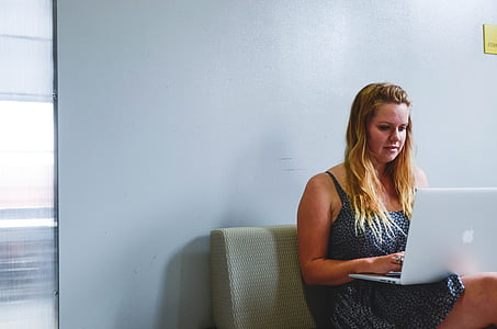 woman wearing grey dress while sitting in couch and using laptop thumbnail