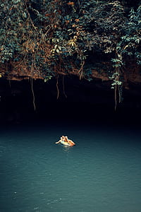 person lying on floater on body of water under cave at daytime thumbnail