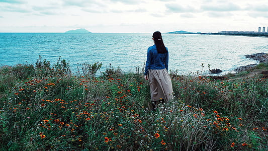 woman standing in orange flower field in front ocean thumbnail