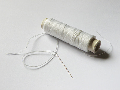 white thread with spool on white surface thumbnail