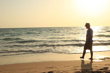 silhouette photography of person in blue shirt and beige fedora cap standing on seashore during golden hour thumbnail