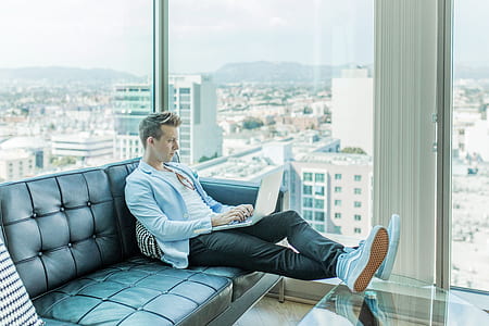 man resting foot at glass coffee table while using laptop thumbnail