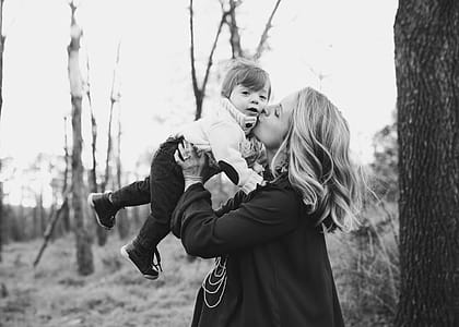Grayscale Photo Of Woman Kissing Toddler On Cheek thumbnail