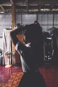 tilt-shift lens photography of woman holding her hair while standing in a dark room thumbnail