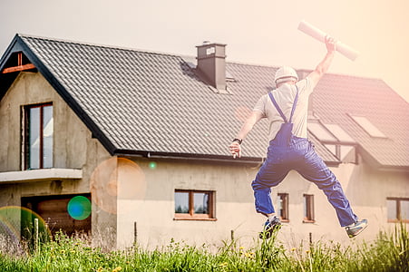 man wearing blue dungaree pants across brown house thumbnail