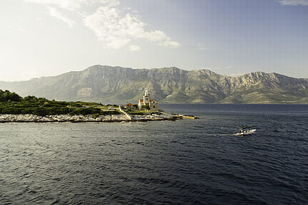 white painted house beside sea with mountain background thumbnail