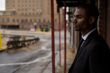 man wearing black suit standing near red pole thumbnail