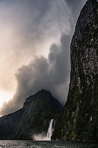 waterfalls flowing towards ocean from mountain covered with clouds thumbnail
