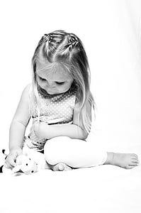 grayscale photo of girl holding plush toy while sitting thumbnail
