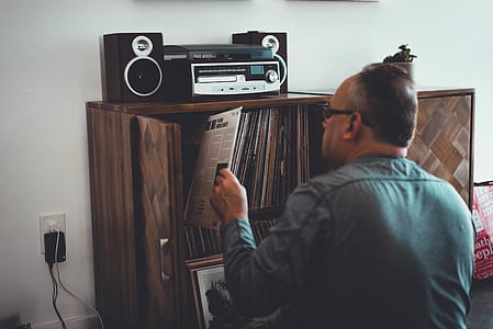 Man in Gray Longsleeve Shirt Holding Book in Front of Brown Wooden Book Case thumbnail