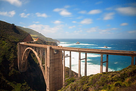 brown bridge between mountain near sea thumbnail