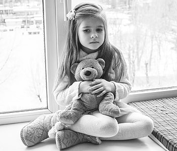 grayscale photo of girl carrying bear plush toy thumbnail
