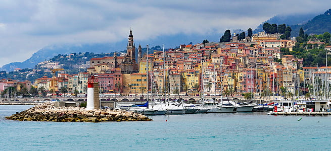 Houses Near With Sea With Sailboats and Lighthouse during Daytime thumbnail