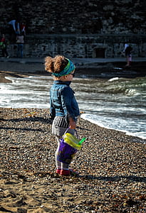 girl holding sand bucket standing on beach front thumbnail
