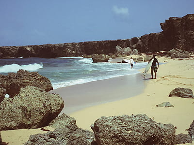 man holding surfboard walking on seashore thumbnail