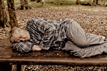 man in black pants sleeping on brown bench thumbnail