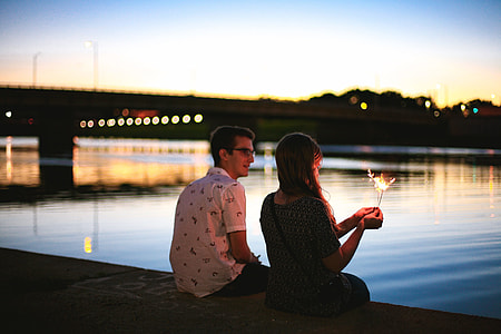 man and woman sitting beside river near bridge during sunset thumbnail