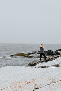 woman wearing gray tank top and black leggings standing on boulder near body of water thumbnail