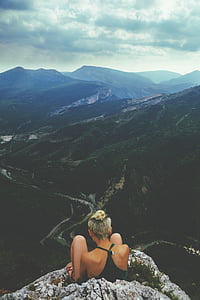 woman wearing black halter top sitting on gray hill in front of mountains thumbnail