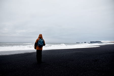 man wearing hooded jacket standing near body of water thumbnail