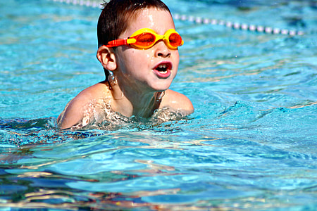 boy wearing orange and yellow diving goggles while swimming on body of water during daylight thumbnail