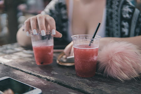 woman in black and white top holding clear plastic cup with red liquid thumbnail