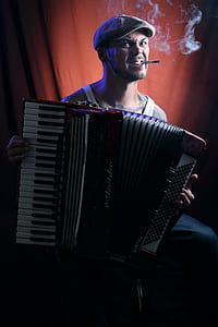 man wearing white tank top holding black accordion thumbnail