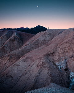 silhouette photo of person standing on top of mountain under crescent moon thumbnail