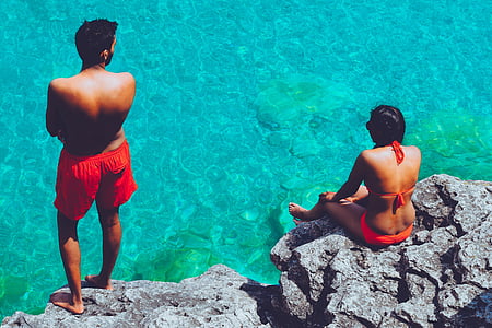 woman sitting beside man standing on rock formation thumbnail