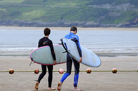 two men walking near shoreline carrying surfboards thumbnail