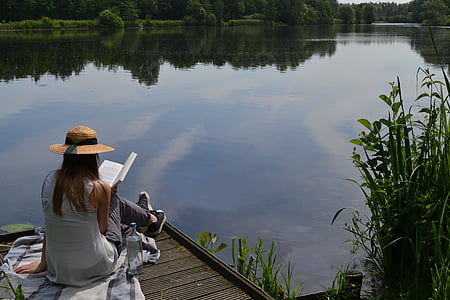 woman in gray sleeveless top reading book beside sitting on dock during daytime thumbnail