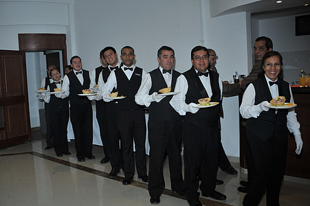 waiters forming line while holding plate with foods beside white wall thumbnail