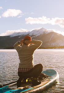 person wearing brown sweater and black and white pants sitting on brown and white paddle board on shore during daytine thumbnail