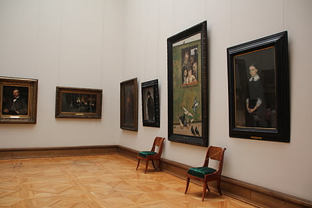 two brown wooden chairs near wall with hanged paintings thumbnail