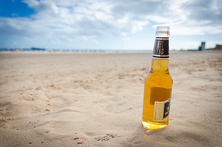 clear glass beer bottle on sand under cloudy sky thumbnail